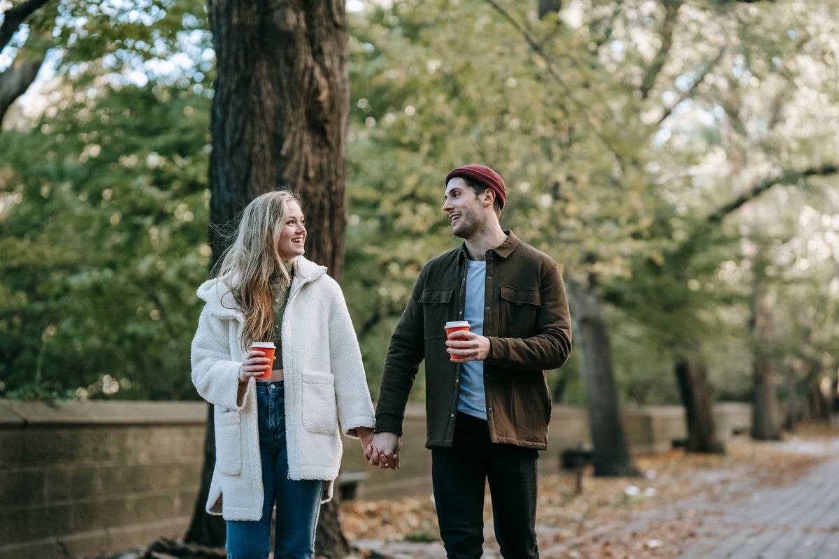 Pareja caminando por un parque con vasos de café
