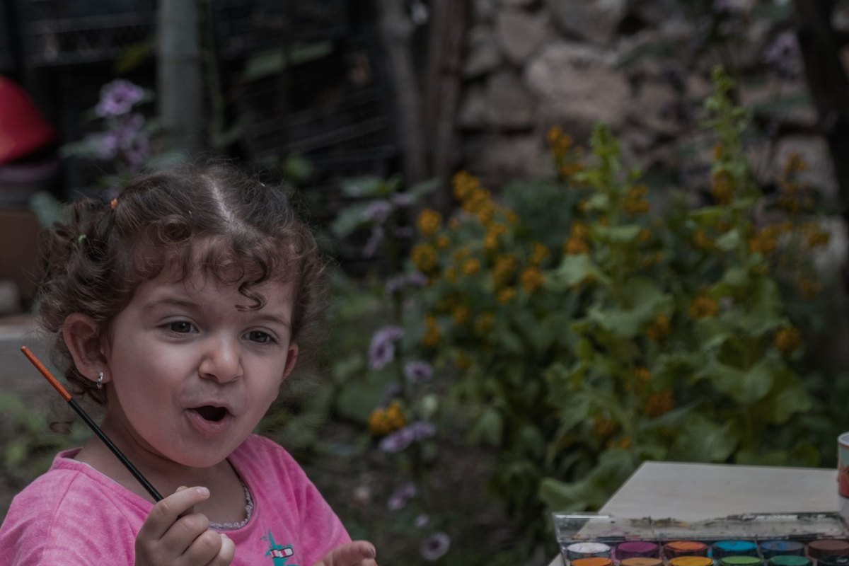 Niña pintando un dibujo con un pincel en un jardín