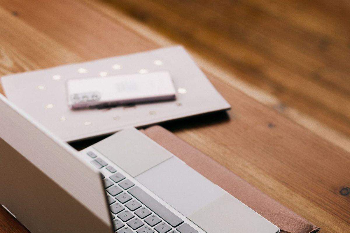 Laptop plateada abierta sobre una mesa de madera junto a un cuaderno